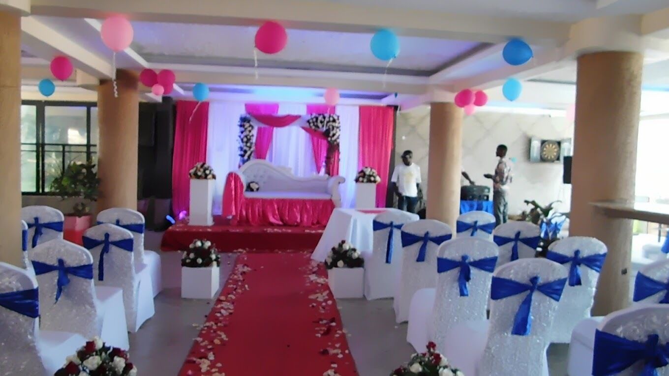 Een bruiloftlocatie met een rode loper, witte stoelen met blauwe linten en een podium met roze gordijnen.