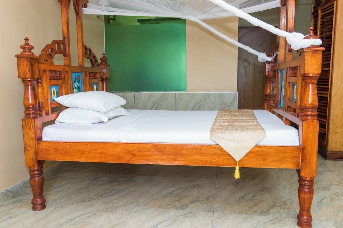 A wooden four-poster bed with white bedding, a beige throw blanket, and a yellow tassel.
