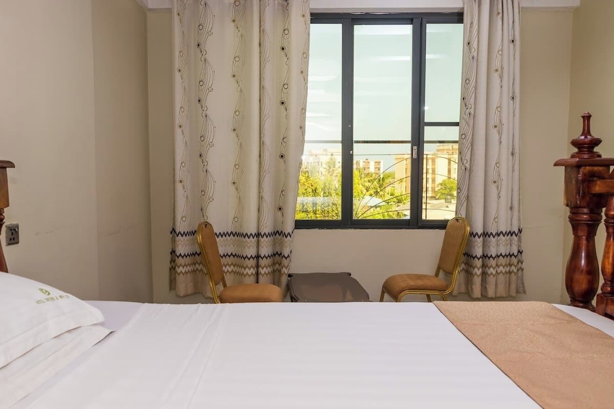 A hotel room with a bed, two chairs, a small table, and a window with curtains.
