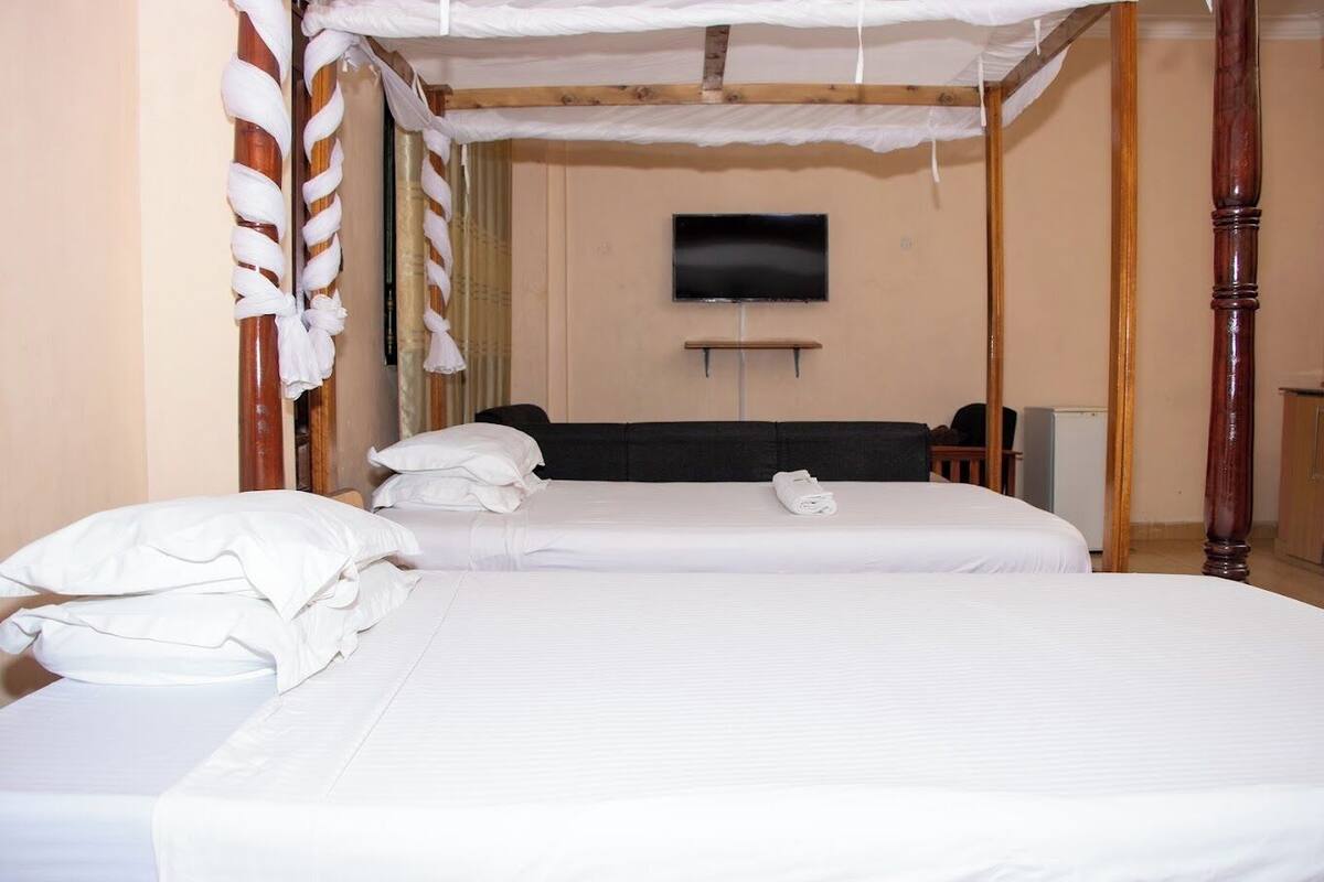 A hotel room with two beds, a television, and a wooden wardrobe.