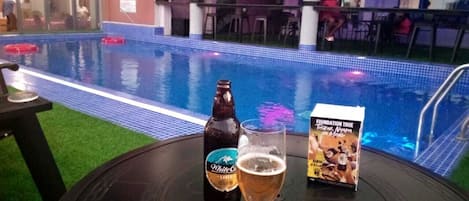 A poolside area with a table, a bottle of beer, and a glass of beer.