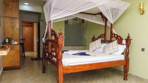 Una cama con dosel de madera con cuatro columnas, un escritorio con hervidor y una silla en una habitación con suelo de baldosas.