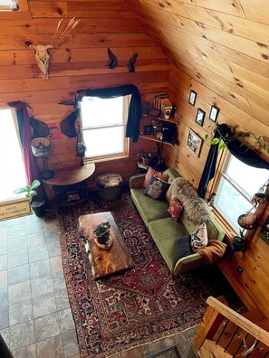 A cozy cabin interior with a wooden ceiling, a green sofa, a patterned rug, and a rustic decor including a skull and wings. - Private Rustic Cabin Near Smuggs • Cozy, Quiet, Pet Friendly (Waterville)