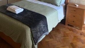 Yhden hengen sänky, jossa on puinen pääty, yöpöytä, jossa on kaukosäädin, ja kalanruotokuviollinen puulattia.