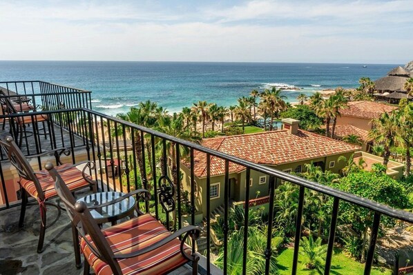 Balcón con sillas y una mesa con vista a la playa y al océano.