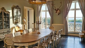 Ein Esszimmer mit einem großen Holztisch, verzierten Stühlen, einer Chandelierleuchtre und einem an der Wand befestigten Hirschkopf.