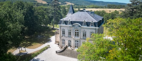 A large, historic building with a symmetrical facade, a central staircase, and a paved courtyard.