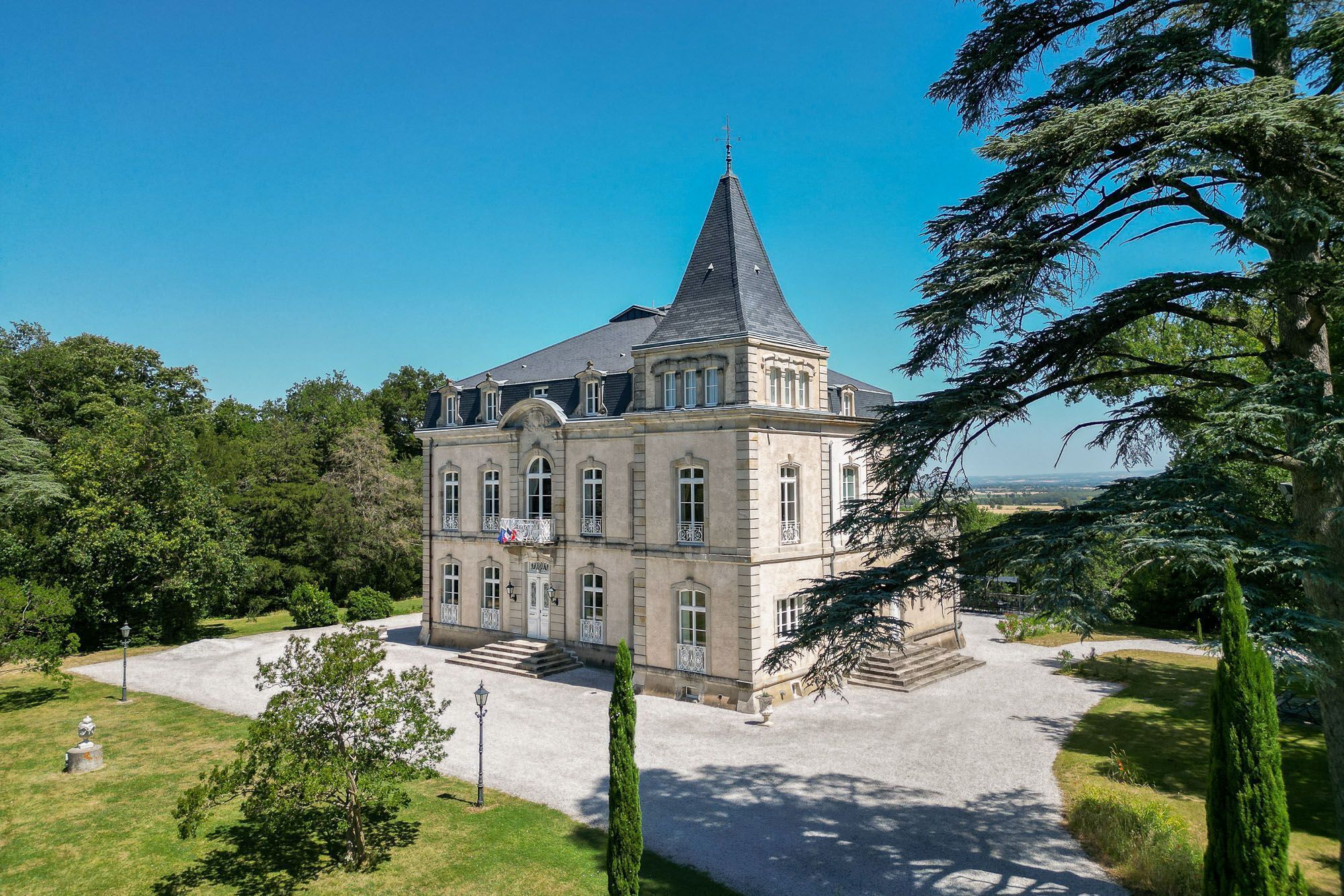 A large, historic building with a prominent tower, surrounded by a well-maintained garden and trees.