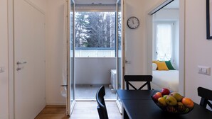 An open door leading to a balcony with a view of trees, a dining table with chairs, and a fruit bowl. - notaMI - Civitali Suite - San Siro (Milan)