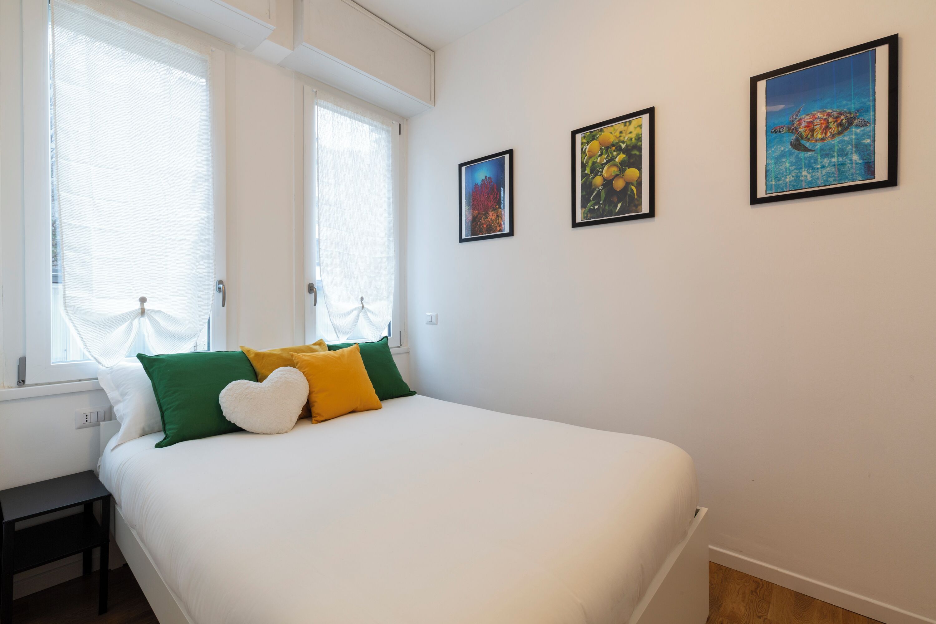 A bedroom with a bed, pillows, a nightstand, and three framed pictures on the wall.