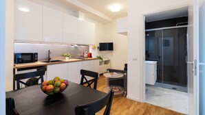A modern kitchen with white cabinets, a black countertop, and a dining area with a black table and chairs. - notaMI - Civitali Suite - San Siro (Milan)