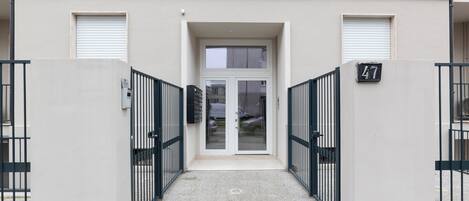 A building entrance with a gated driveway, a number '47' sign, and a door with a window above it.