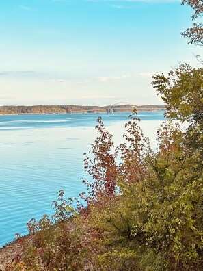 A calm lake with a bridge in the distance and trees in the foreground.