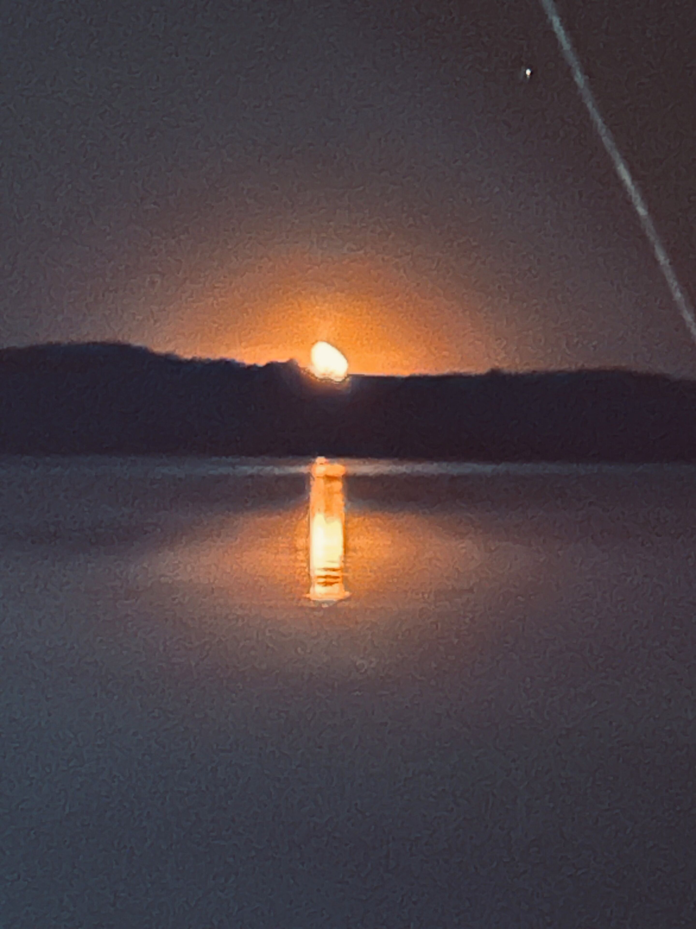 A nighttime scene with a full moon reflecting on a calm body of water.