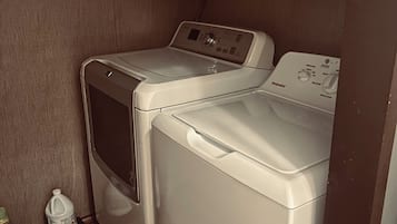 A laundry area with two front-loading washing machines, a wooden floor, and a wall-mounted cabinet above the machines.