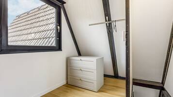 Une pièce avec une fenêtre, une commode blanche et un plafond en pente.