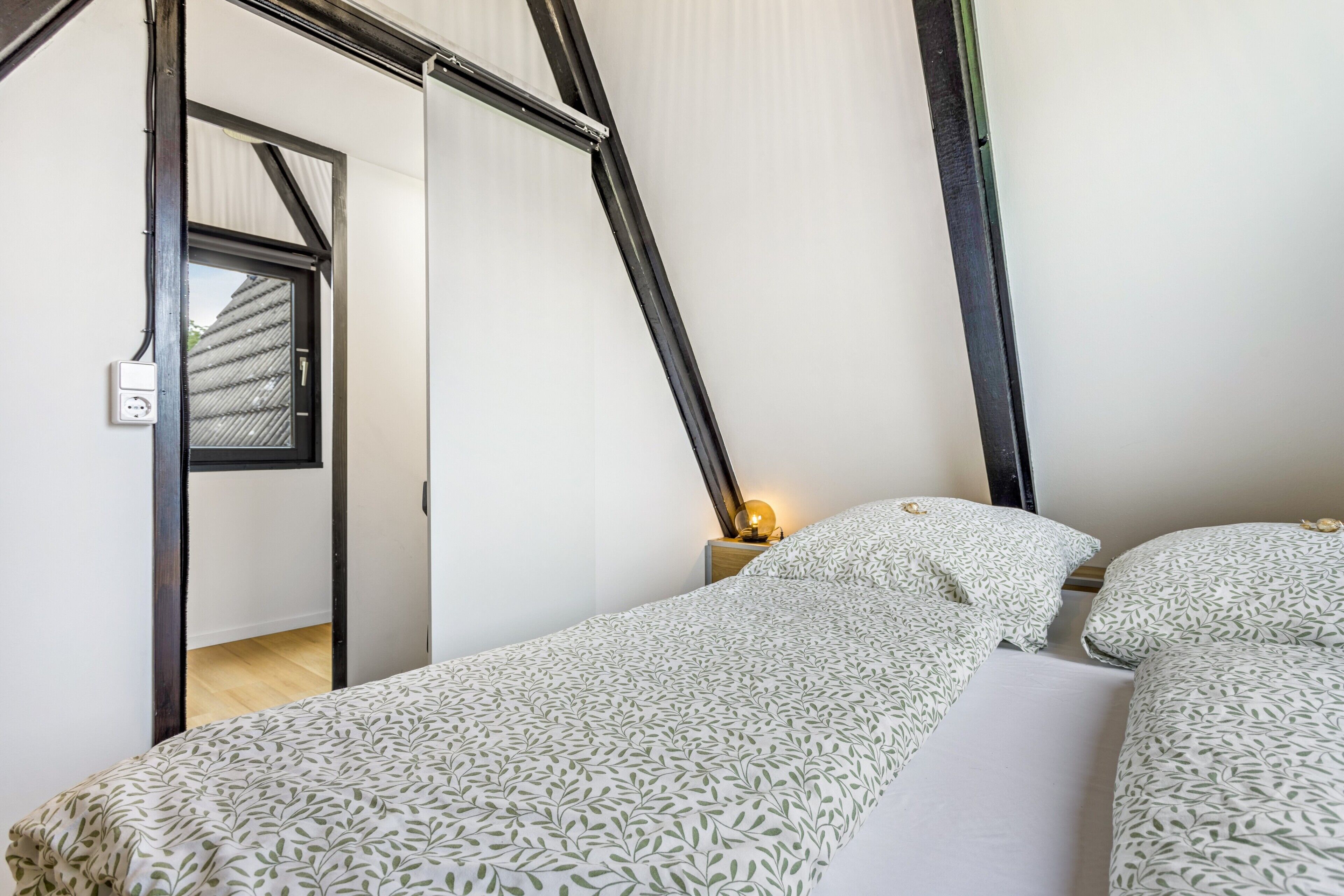 A room with a bed, a nightstand, a lamp, and a window with a view of a building.