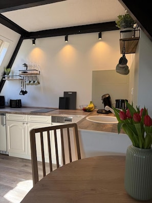 Une cuisine moderne avec une table à manger en bois, un vase de tulipes et une plante suspendue.