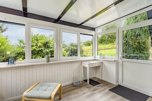 A conservatory with large windows, a wooden bench, a small table, and a radiator.
