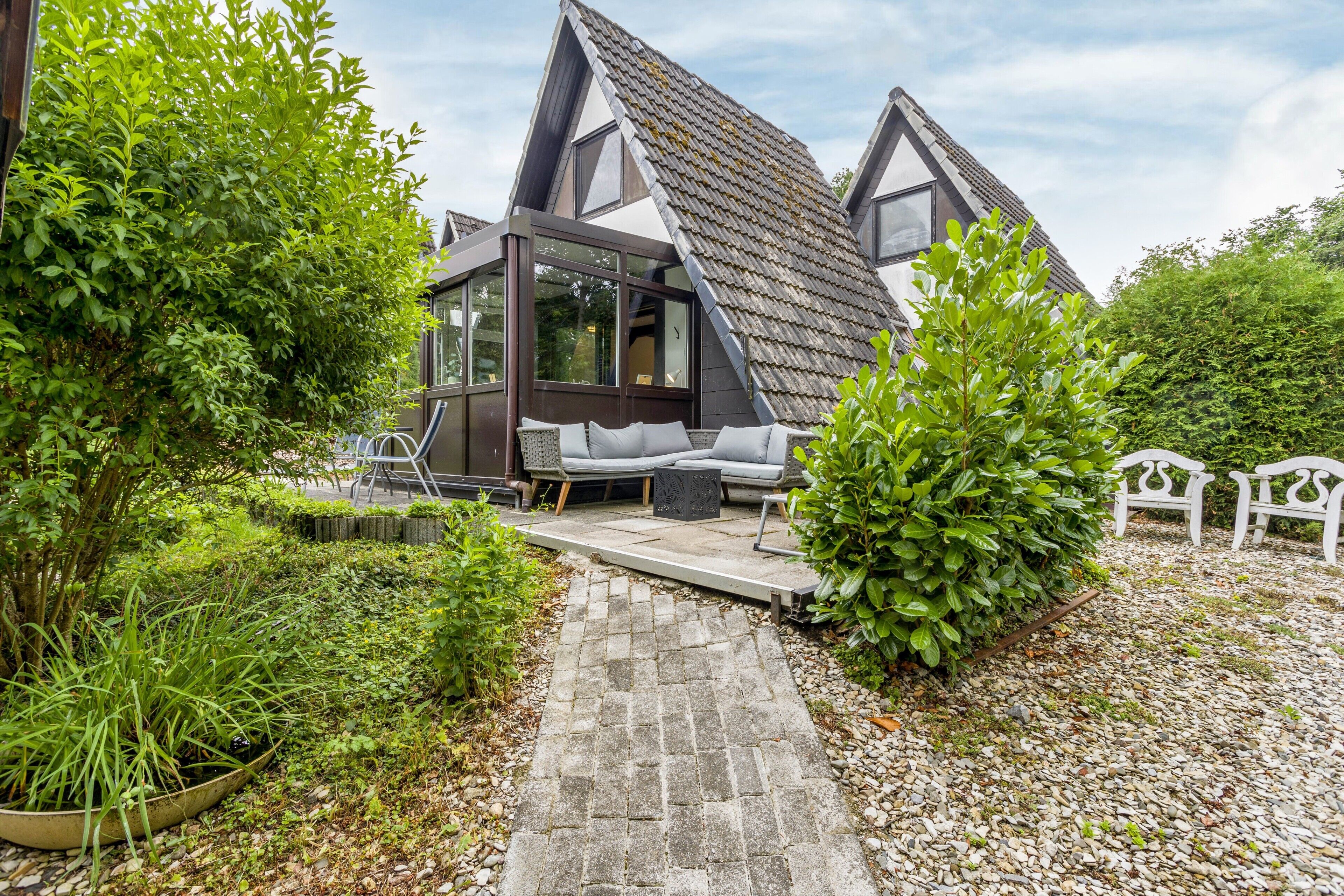 Een modern huis met een schuin dak, een terras met tuinmeubilair en een tuin.