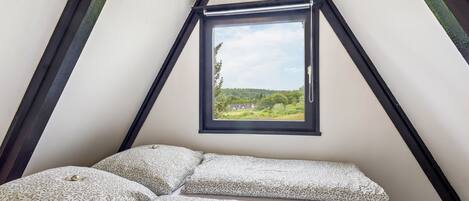 A bedroom with a bed, pillows, and a window with a view of greenery.