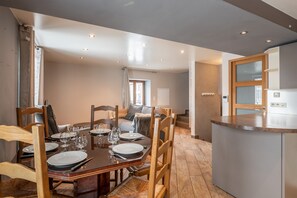 A dining area with a wooden table set for four, a kitchen with a grey countertop, and a staircase leading to another level. - Apartment 'Loft Cosy Au Coeur Du Village' with Mountain View and Wi-Fi (Villard-de-Lans)