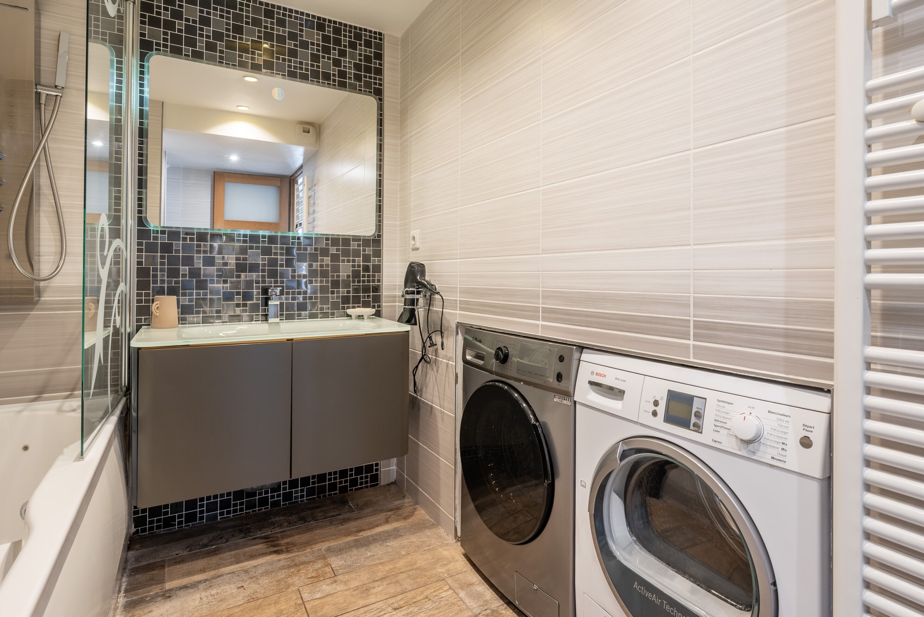 Une salle de bain compacte dotée d’une douche à parois de verre, d’un lave-linge encastré et d’un pare-feu en carrelage.