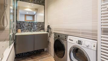 Une salle de bain compacte dotée d’une douche à parois de verre, d’un lave-linge encastré et d’un pare-feu en carrelage.