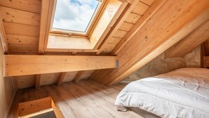 Ein Schlafzimmer im Dachgeschoss mit Holzboden, einem Schimmerfenster, einem Bett und einem kleinen Holzschrank.