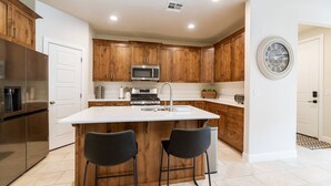 A modern kitchen with wooden cabinets, a stainless steel refrigerator, a microwave, a sink, and two bar stools. - Spacious Getaway w/Heated Pool (Washington)