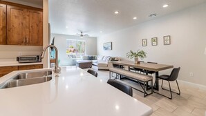 A modern kitchen with a central island, a dining area with a wooden table and benches, and a living room with a sofa and a large window. - Spacious Getaway w/Heated Pool (Washington)
