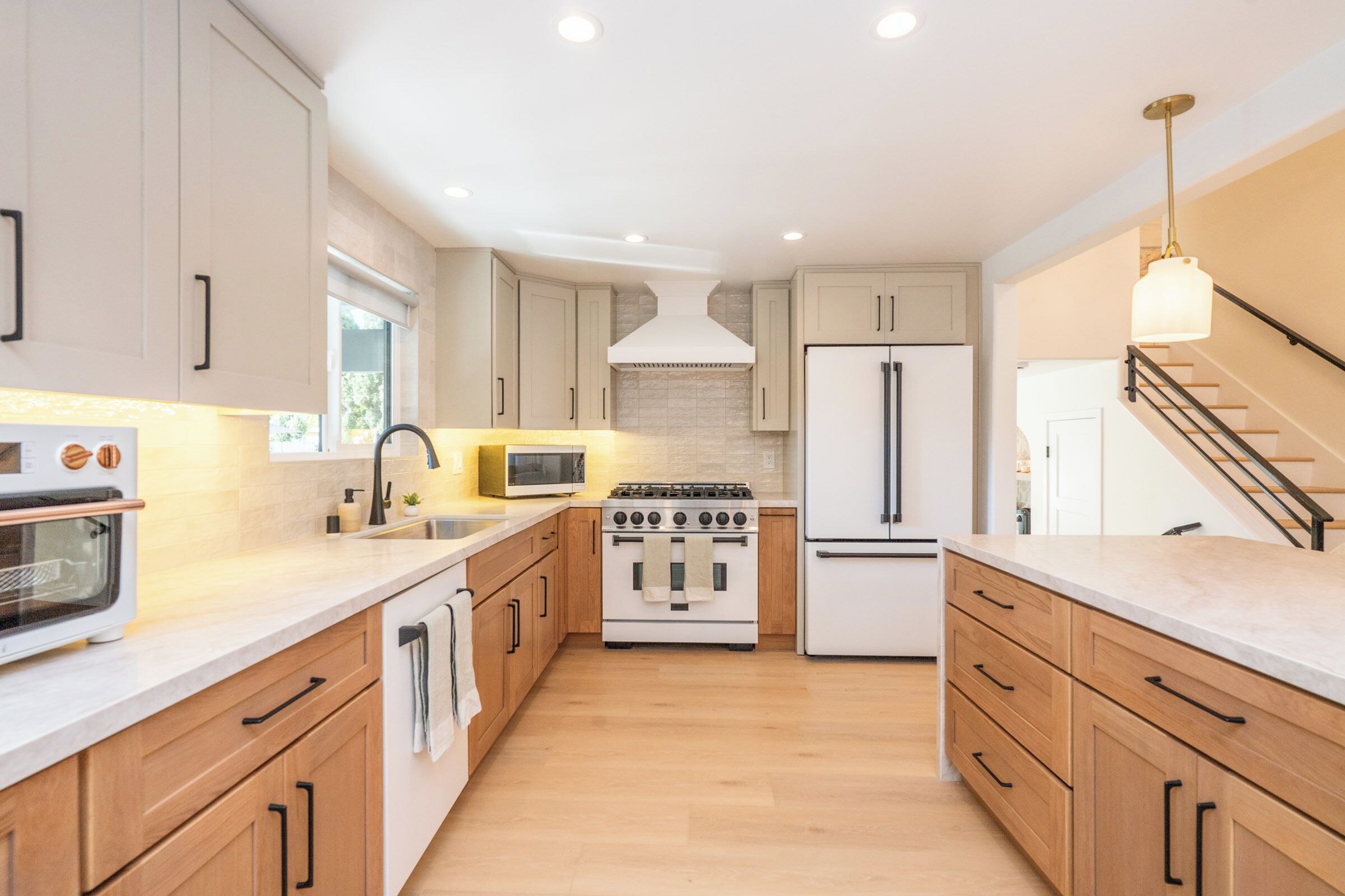 A modern kitchen with wooden cabinets, a stainless steel refrigerator, a microwave, an oven, and a gas stove.