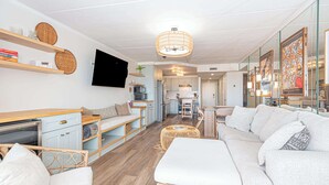 Un salon moderne avec un canapé, un téléviseur, une cuisine en arrière-plan et un coin repas.