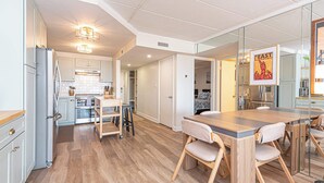 Une cuisine moderne dotée d’un îlot central, d’un coin repas avec une grande table et d’un mur miroir qui agrandit visuellement l’espace.