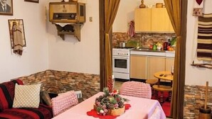 Un salon chaleureux avec une table à manger dressée pour deux personnes, une cuisine en arrière-plan et un mur d’accent en pierre.
