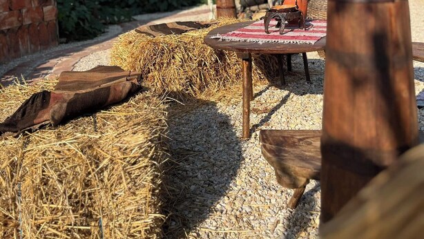 Un espace de restauration extérieur rustique, avec des bottes de foin, une table en bois et une clôture en métal.