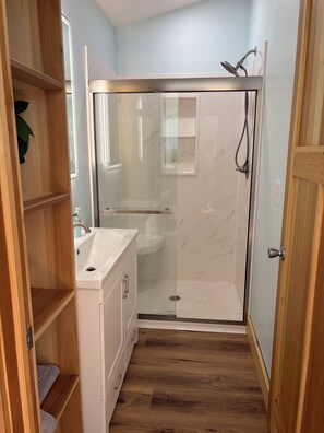 Un baño con ducha, lavamanos y estanterías de madera.