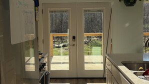 Une cuisine avec une porte double donnant sur une terrasse, un réfrigérateur et une plante suspendue.