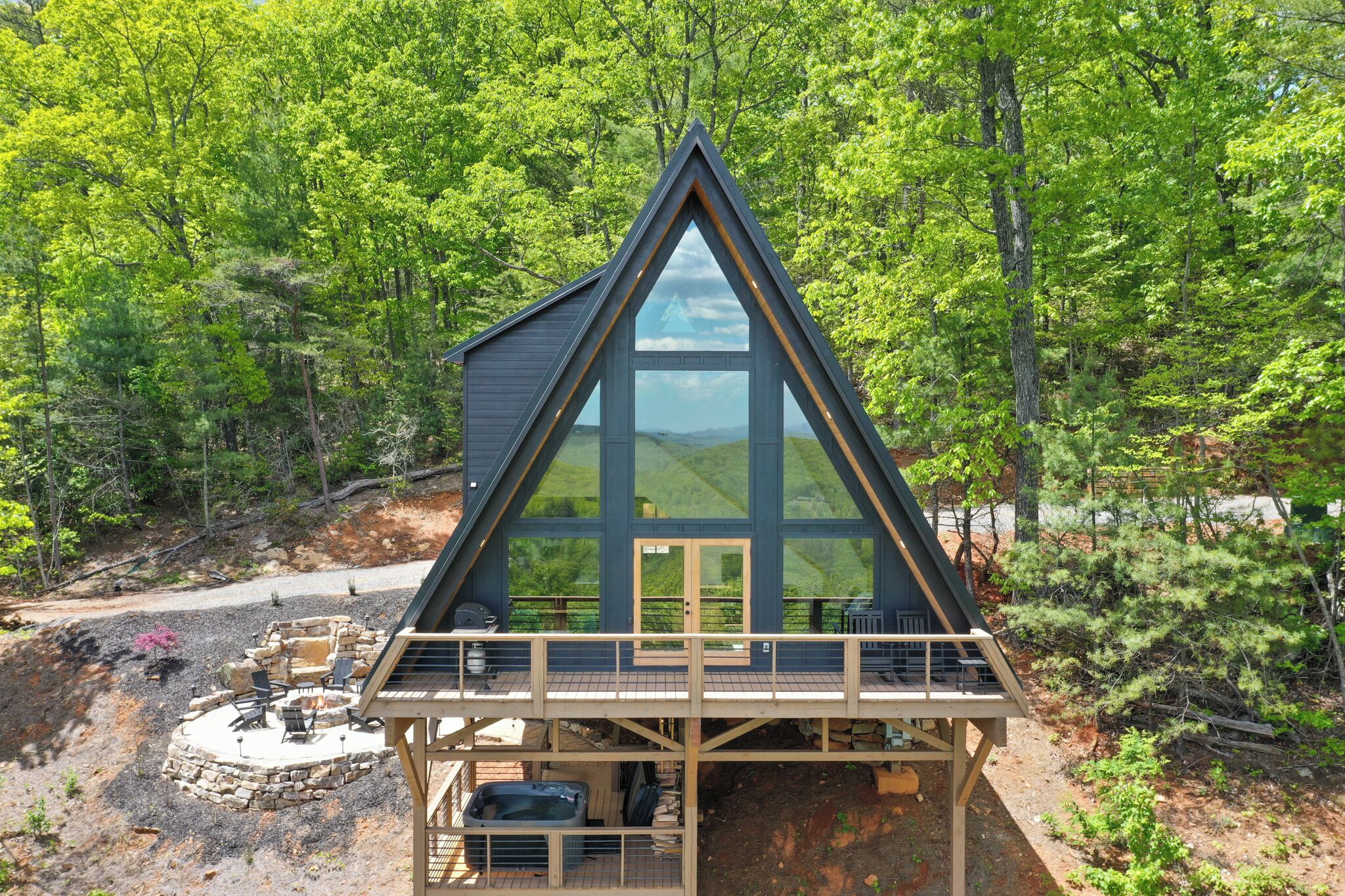 A triangular cabin with a large glass window, a deck, and a stone fire pit area.