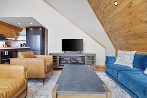 Un espace de vie de style loft doté d’une cheminée, de canapés en cuir, d’un téléviseur à écran plat et de poutres apparentes en bois au plafond.
