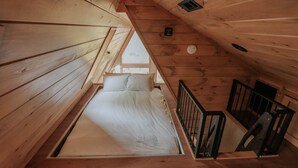 Un interior de madera con una cama, una ventana y una escalera.
