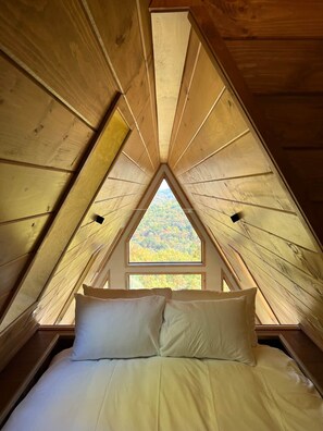 Une chambre mansardée triangulaire, avec un lit, des oreillers et une fenêtre.