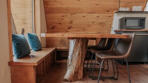 Un banco de madera con cojines, una mesa de tocón rústico y una zona de cocina con microondas.