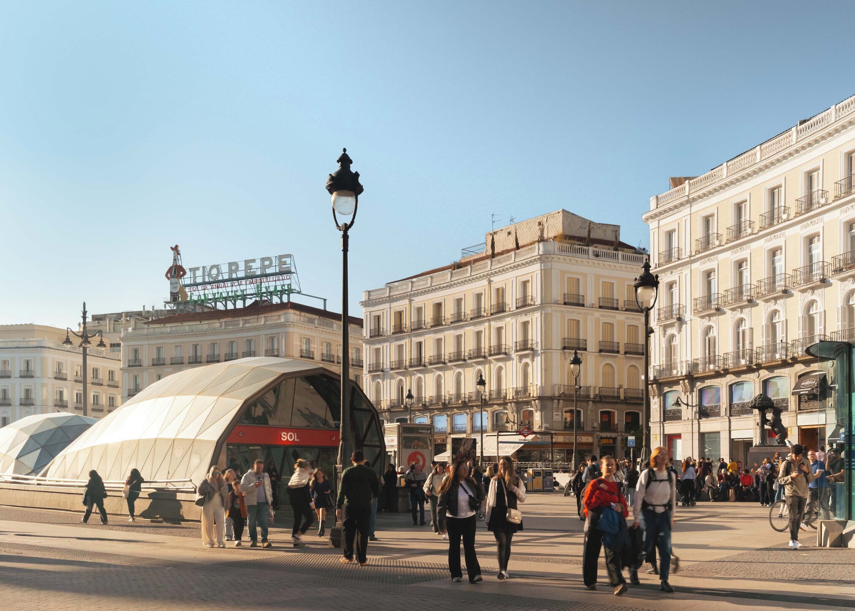 Una animada plaza urbana con edificios históricos, una estructura cubierta y un letrero destacado.