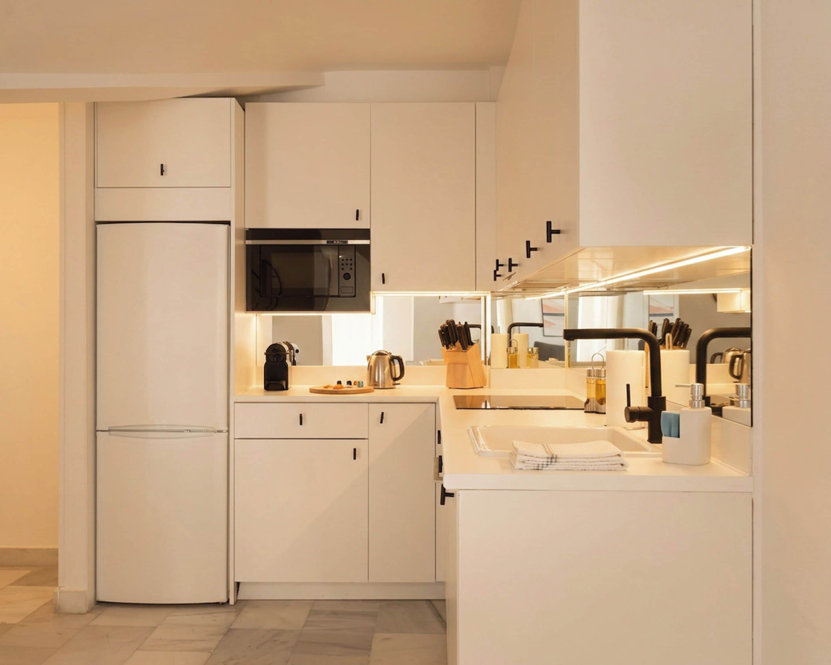Een moderne keuken met witte kasten, een ingebouwde magnetron, een koelkast en een gootsteen met een kraan.