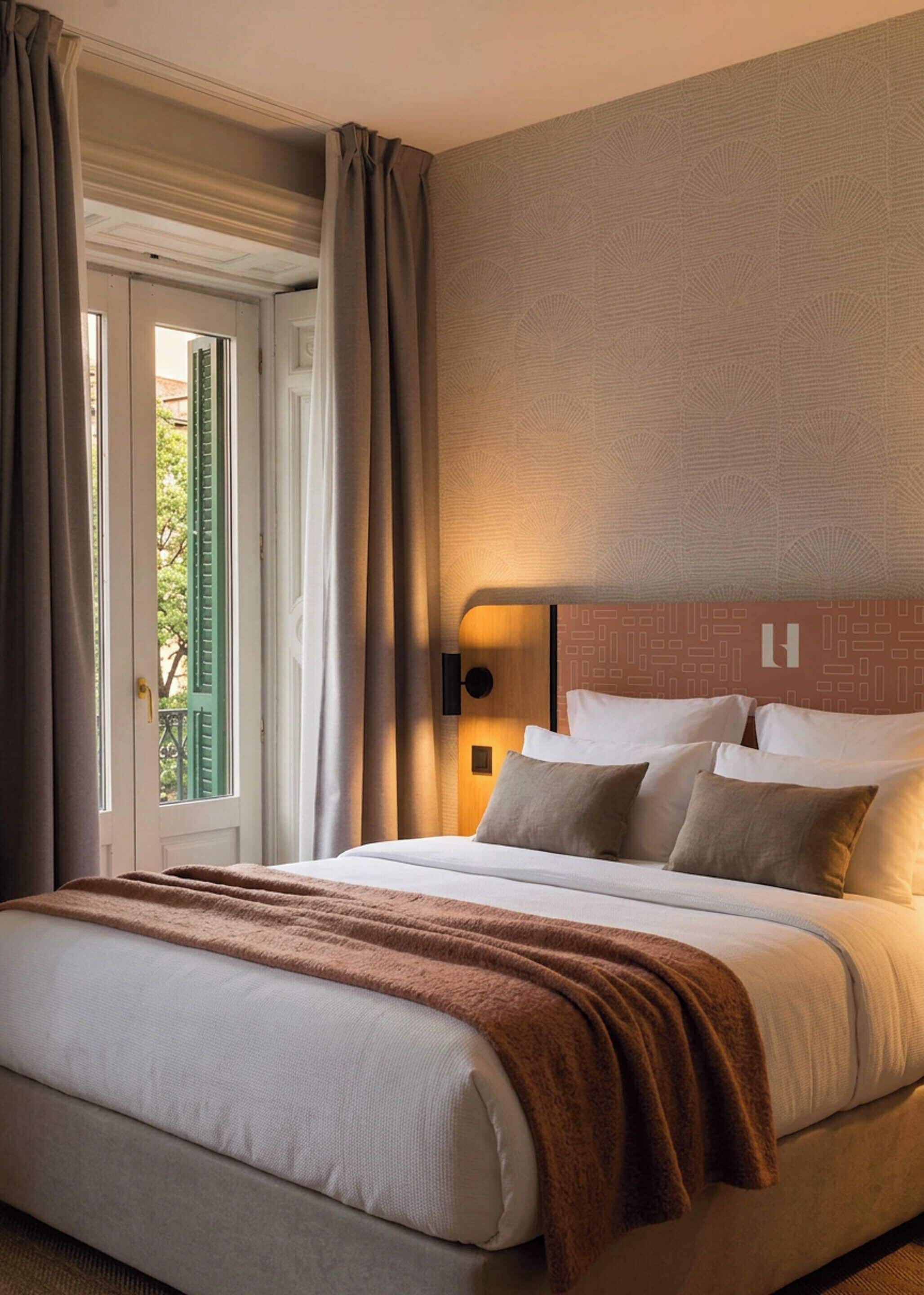 Habitación de hotel con cama, cortinas, una lámpara de pared y vistas a través de una ventana.