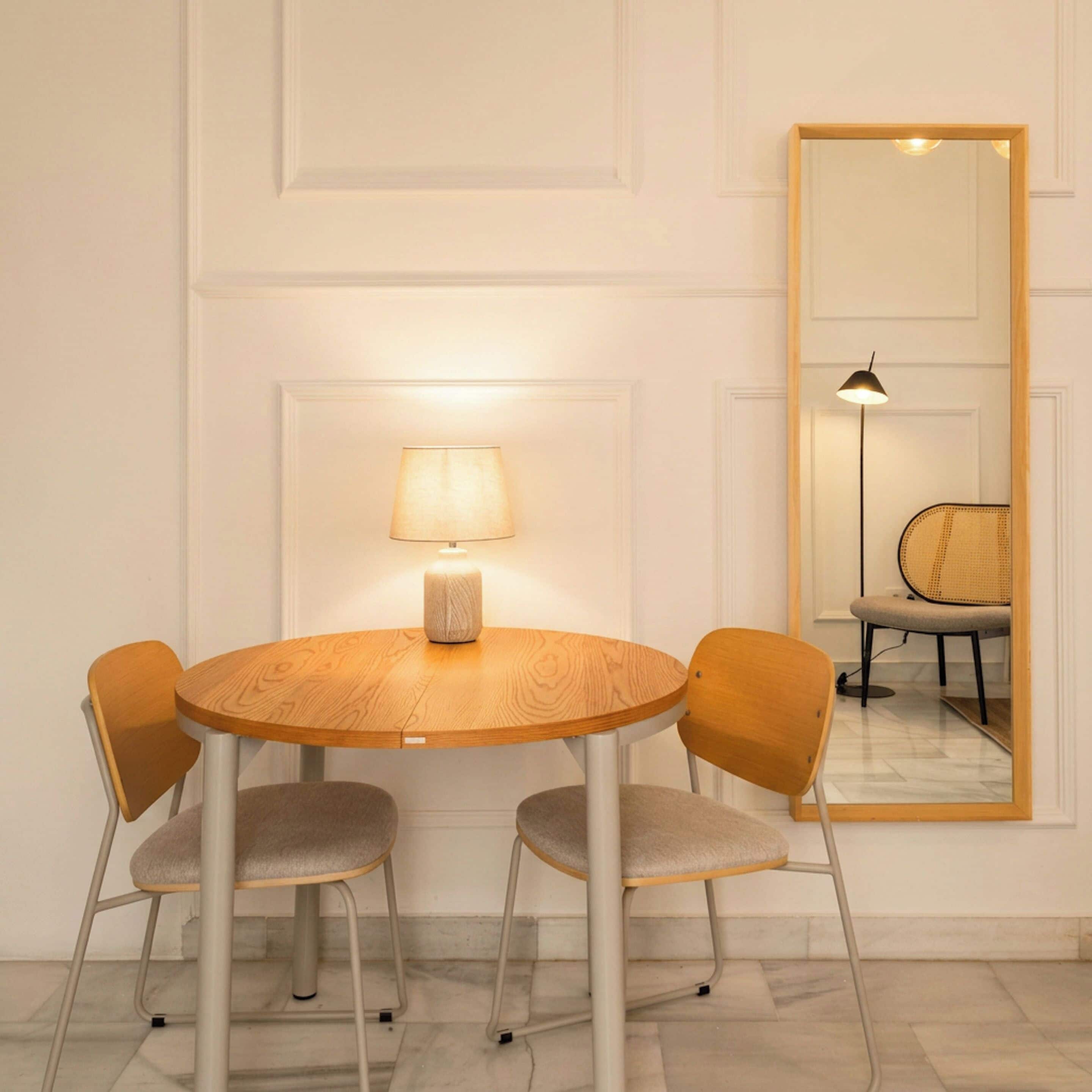 Una mesa redonda de madera con dos sillas, una lámpara y un espejo en la pared.