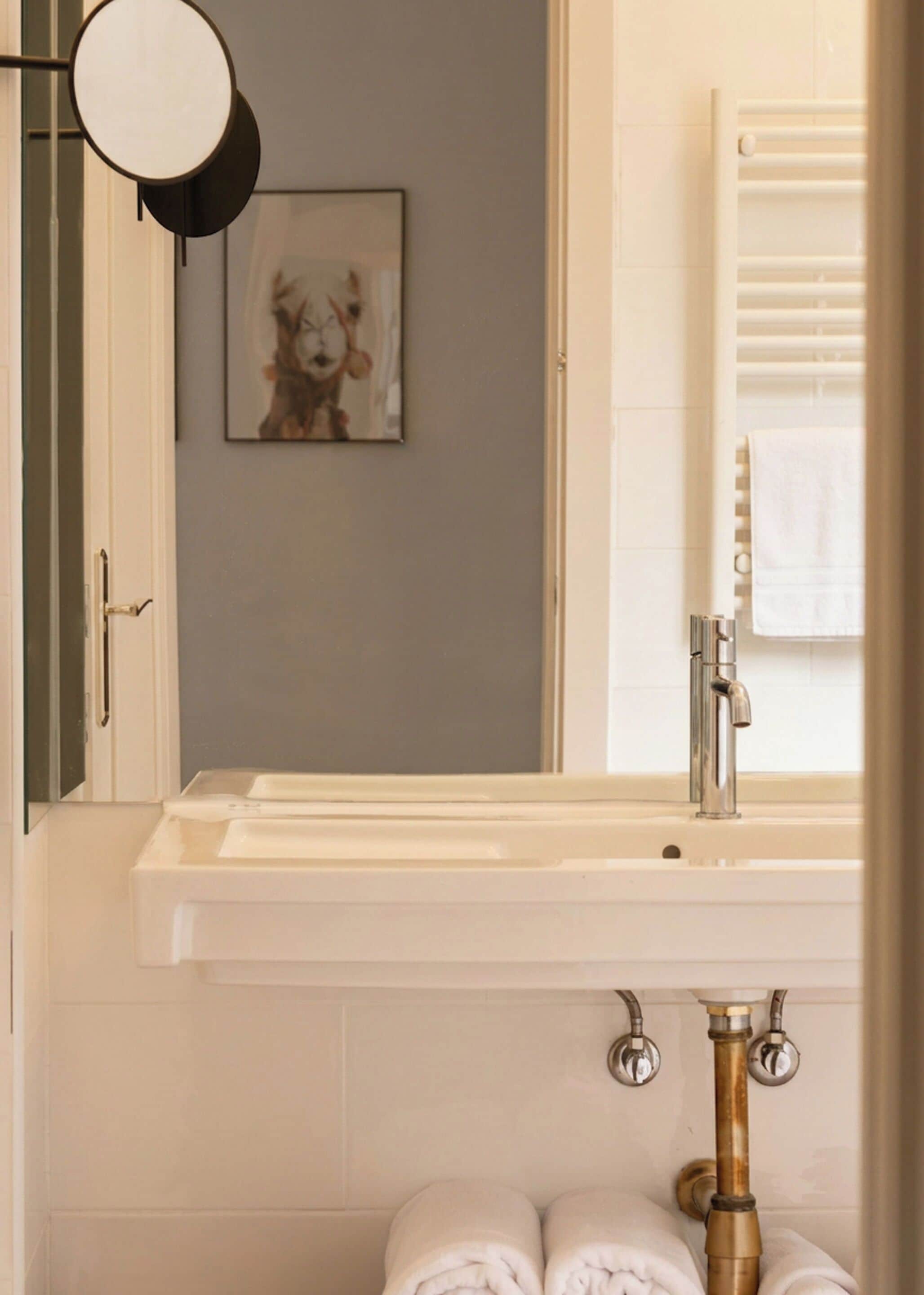 A bathroom with a white sink, a mirror, a towel rack, and a framed picture on the wall.