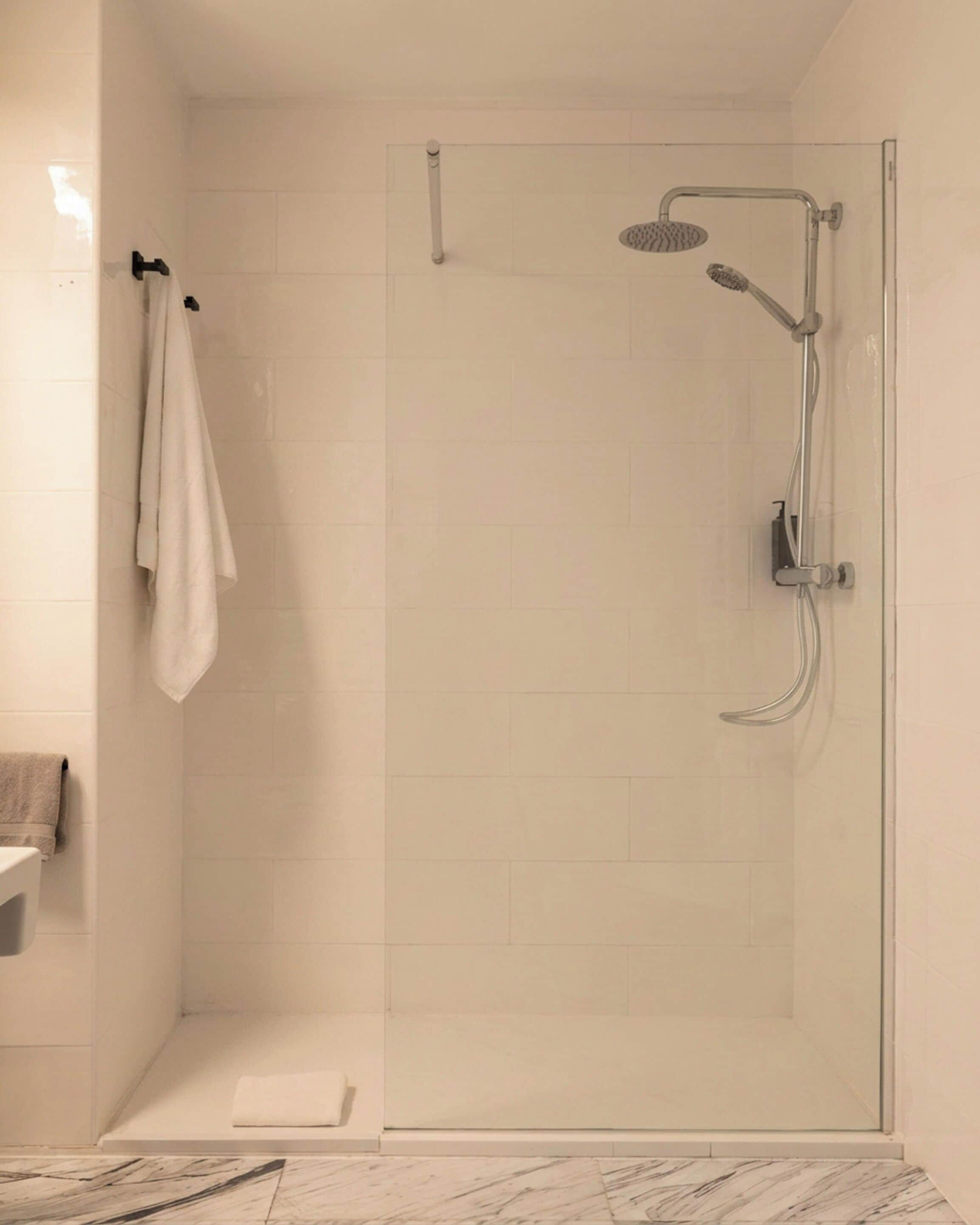A glass-enclosed shower with a handheld showerhead and a wall-mounted faucet.