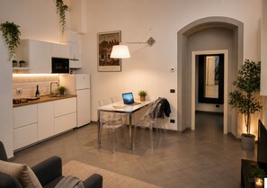 A modern kitchen with white cabinets, a dining area with clear chairs, and a laptop on the table. - Red Door Dream App. 3 (Firenze)